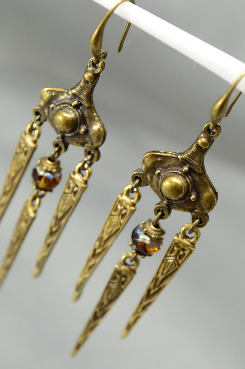 May include: Gold tone dangle earrings with three teardrop-shaped charms and amber-coloured glass beads.