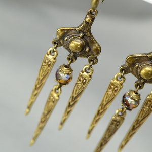 May include: Gold tone dangle earrings with three pointed, ornate drops and a single iridescent bead on each earring.