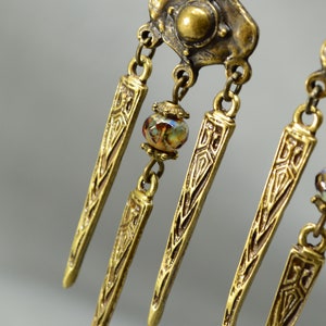May include: Gold tone dangle earrings with a geometric design and a single iridescent glass bead.