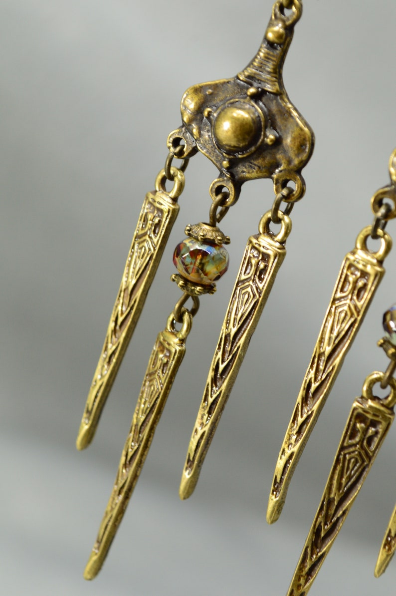 May include: Gold tone dangle earrings with a geometric design and a single iridescent glass bead.