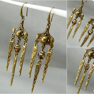 May include: A pair of gold-toned dangle earrings with three pointed teardrop-shaped charms and a small round bead on each earring.
