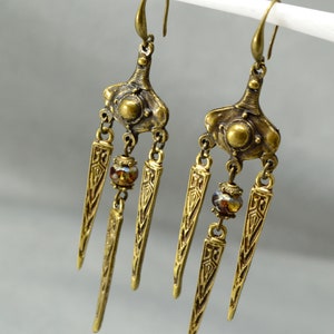 May include: A pair of gold-tone dangle earrings with a geometric design and brown glass beads. The earrings have a long, pointed shape and are suspended from a hook.
