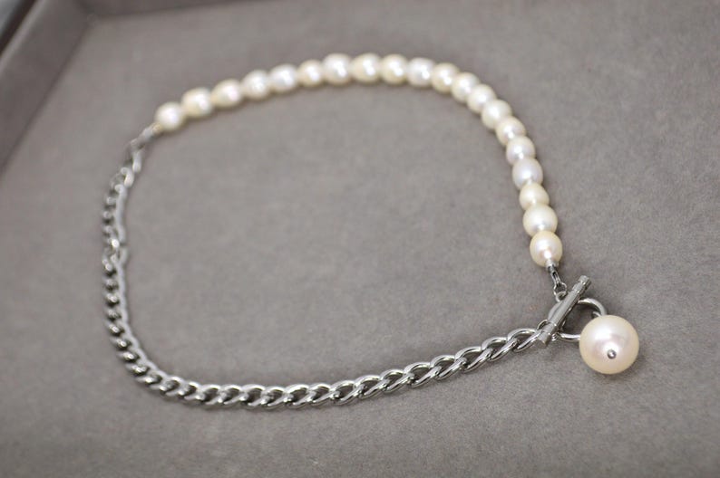 May include: A necklace featuring a combination of pearls and a silver chain. The necklace has a toggle clasp with a single pearl pendant. The pearls are white and the chain is a curb style.