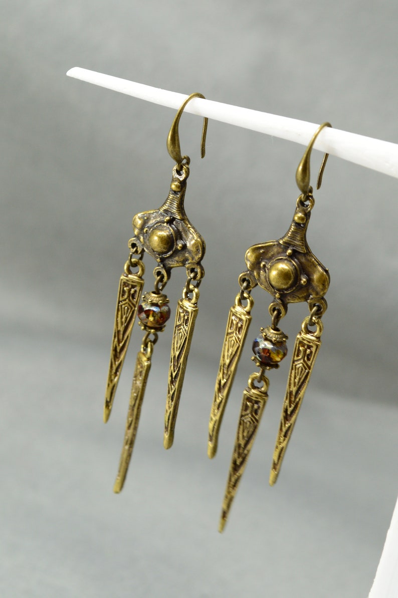 May include: A pair of gold-tone dangle earrings with three teardrop-shaped pendants and a small round bead on each earring.