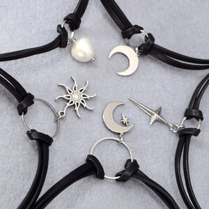 May include: Black leather choker necklaces with silver-tone celestial charms. The charms include a pearl, crescent moons, a sun, and a star. The necklaces are displayed on a gray surface.