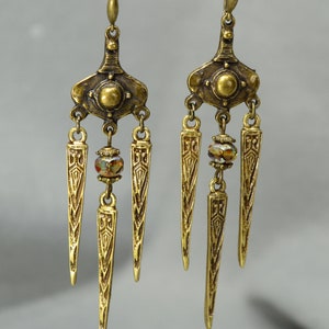 May include: Gold tone dangle earrings with three pointed teardrop shapes and a crystal bead on each earring.