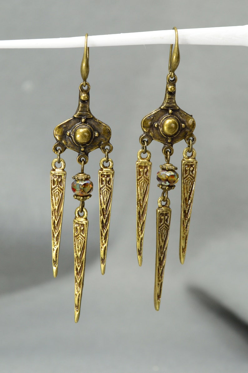 May include: Gold tone dangle earrings with three pointed teardrop shapes and a crystal bead on each earring.