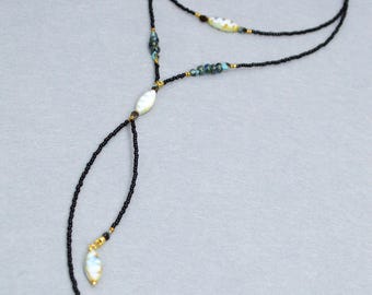 May include: A delicate necklace featuring a black beaded chain with gold accents. The necklace has a Y-shaped design with a central oval bead and two teardrop-shaped pendants. The beads are a mix of black, gold, and iridescent colors.