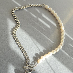 May include: A necklace featuring a combination of a silver chain and a strand of white pearls. The necklace has a toggle clasp and a single pearl pendant. The design is modern and elegant, suitable for various occasions.