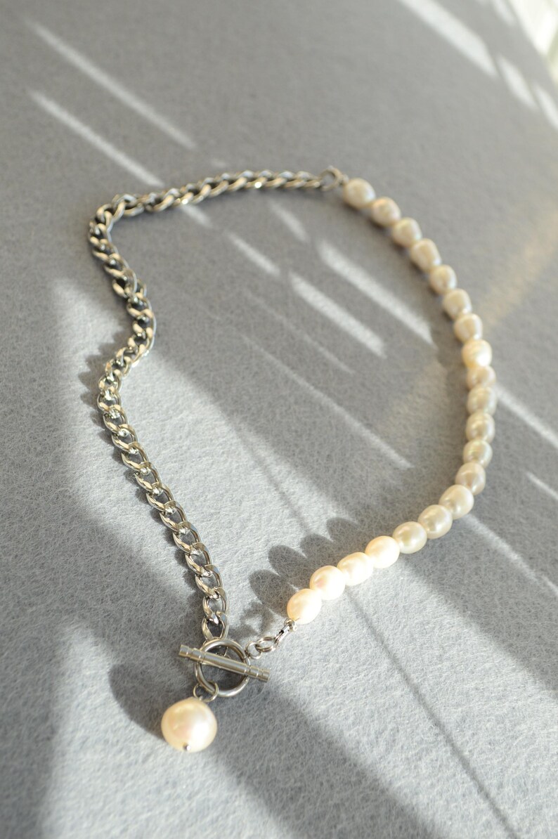 May include: A necklace featuring a combination of a silver chain and a strand of white pearls. The necklace has a toggle clasp and a single pearl pendant. The design is modern and elegant, suitable for various occasions.