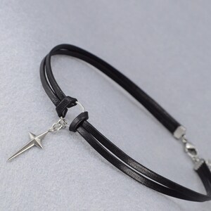 May include: Black leather choker necklace with a silver-tone star pendant. The choker features a double-strand design and a clasp closure. The star pendant is a four-pointed star with a pointed tip.