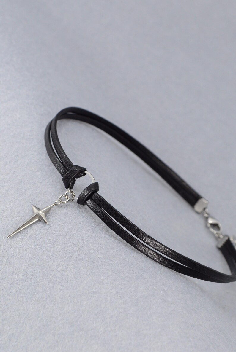 May include: Black leather choker necklace with a silver-tone star pendant. The choker features a double-strand design and a clasp closure. The star pendant is a four-pointed star with a pointed tip.