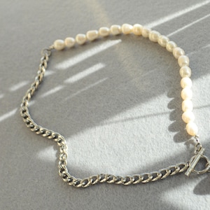 May include: A necklace featuring a combination of pearls and a silver chain. The necklace has a toggle clasp and a single pearl pendant. The pearls are off-white, and the chain is a silver color.