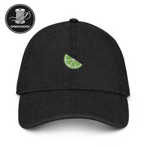 May include: Black baseball cap with a lime slice embroidered on the front. The lime slice is green with white details. The cap has a curved brim and a button on top. The cap has the word "EMBROIDERED" in a circle.