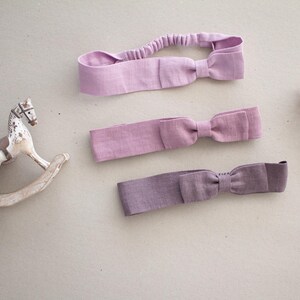May include: Three purple fabric headbands with bows. The headbands are made of a soft, stretchy fabric and are perfect for adding a touch of style to any outfit.