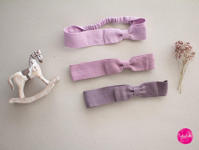 May include: Three purple fabric headbands with bows. The headbands are made of a soft, stretchy fabric and are perfect for adding a touch of style to any outfit.