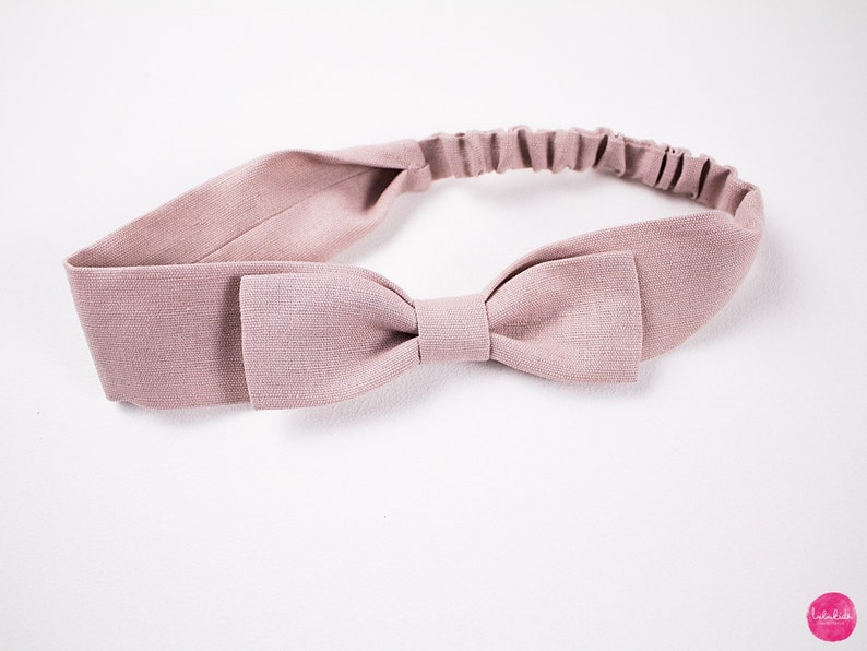 May include: A dusty rose headband with a fabric bow. The headband is made of a soft, stretchy material.