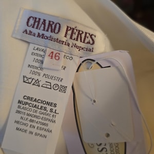 May include: A close-up of a white garment tag with the text "CHARO P&Eacute;RES Alta Modister&iacute;a Nupcial". The tag also includes size 46, washing instructions, and the text "CREACIONES NUPCIALES, S.L. MADE IN SPAIN".