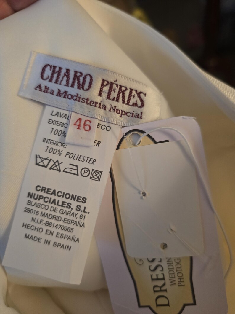 May include: A close-up of a white garment tag with the text "CHARO P&Eacute;RES Alta Modister&iacute;a Nupcial". The tag also includes size 46, washing instructions, and the text "CREACIONES NUPCIALES, S.L. MADE IN SPAIN".