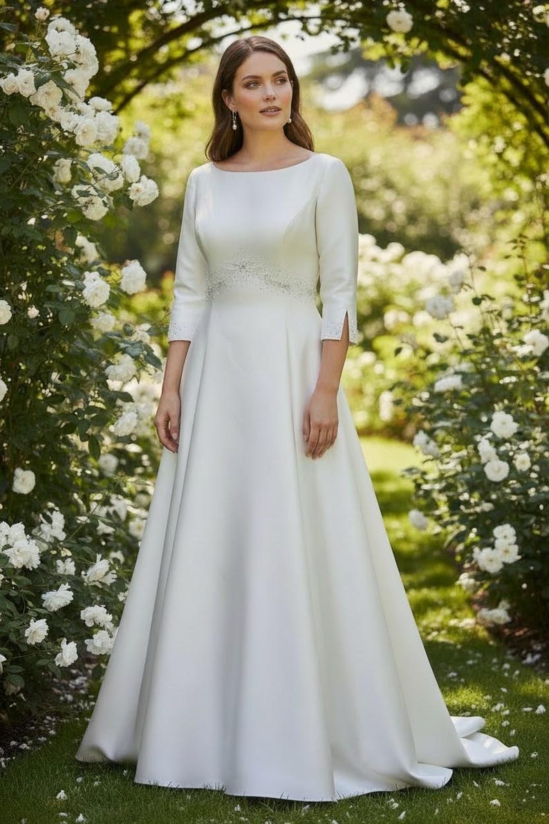 May include: A white wedding dress with a boat neckline and three-quarter sleeves. The dress features a detailed waistline and a flowing A-line skirt. The bride is standing in a garden with white roses.