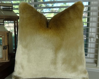 May include: A soft, plush pillow with a light brown faux fur cover. The pillow has a gradient color effect, transitioning from a darker brown to a lighter beige.