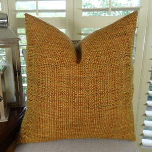May include: A square throw pillow with a woven fabric cover in shades of gold, orange, and brown.