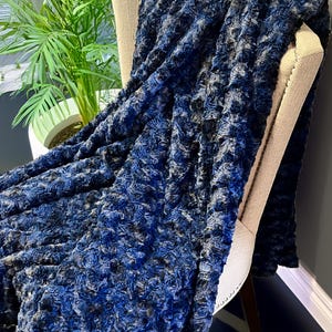 May include: A soft, blue and black faux fur throw blanket draped over a chair. The blanket has a curly, textured pattern.