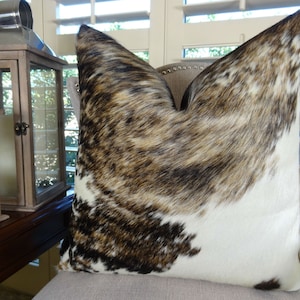 May include: A brown, black and white cowhide cushion with a soft, plush texture. The cushion is made from genuine cowhide and features a unique, natural pattern.