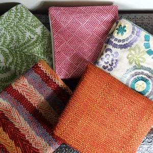 May include: Five different fabric swatches in various colours and patterns. The swatches include a green floral pattern, a red and white geometric pattern, a cream floral pattern with teal and green accents, a red and orange striped pattern, and a solid orange fabric.