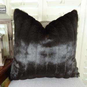 May include: A brown faux fur throw pillow with a square shape. The pillow is made of a soft, plush material and has a subtle sheen.