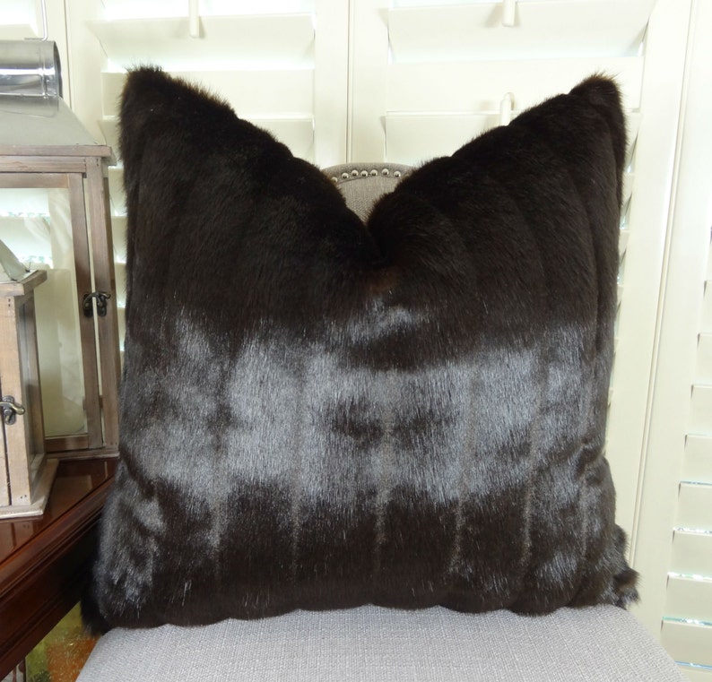 May include: A brown faux fur throw pillow with a square shape. The pillow is made of a soft, plush material and has a subtle sheen.