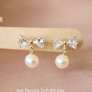 May include: A pair of gold clip-on earrings with a pearl drop and a crystal bow design. Non Piercing CLIP-ON only.