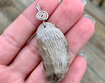 May include: A light gray, oval-shaped pendant made from fossilized coral with a silver wire loop at the top.