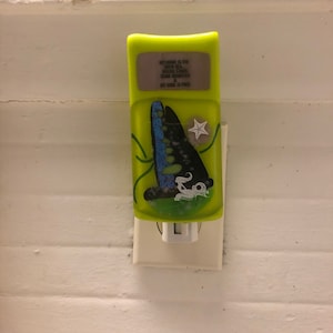 Puede incluir: Un enchufe de luz nocturna verde con un diseño de velero azul y negro y una estrella de mar. El texto en la luz nocturna dice: "My home is the open sea, where stars shine brightest & my soul is free."