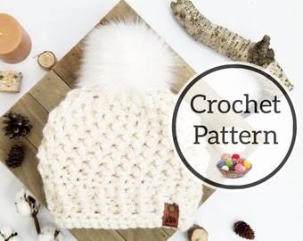 May include: White crochet beanie with a fluffy white pom pom on top. The beanie is laying on a wooden surface with a brown leather tag that says "Made with Love". The image also includes the text "Crochet Pattern" in a circle.