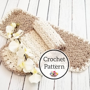 Puede incluir: Dos alfombras ovaladas de crochet en beige y blanco con un borde de crochet. Las alfombras están sobre una superficie de madera blanca con una orquídea blanca.