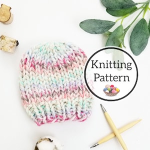 May include: A pink, white, and blue striped knitted hat with knitting needles and a sign that says "Knitting Pattern".