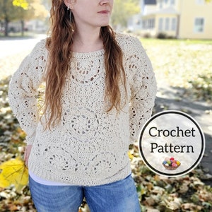Op de afbeelding: Een gebreide trui met een kantpatroon in crèmekleur. De trui heeft een ronde hals en lange mouwen. Het model draagt de trui met een blauwe jeans en staat in een park met herfstbladeren op de grond. De tekst "Crochet Pattern" is zichtbaar in de afbeelding.