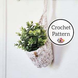 May include: A beige crocheted plant hanger with a small potted plant hanging from a hook on a white wall. The text "Crochet Pattern" is written in a circle with a small image of yarn balls in a basket.