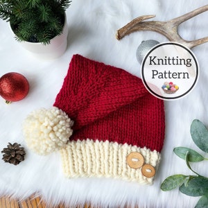 Puede incluir: Un gorro de punto rojo y blanco con un pompón blanco y botones de madera. El gorro está sobre una superficie blanca y esponjosa. Patrón de tejido de punto.