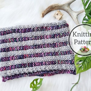 May include: A chunky knit cowl in shades of gray, purple, and pink, with horizontal stripes. The text "Knitting Pattern" is in a circular graphic. The cowl is displayed on a white, fluffy surface.