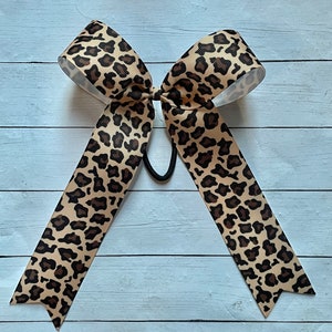 May include: A large brown and black leopard print hair bow with a black elastic band.