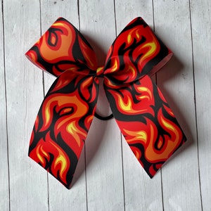 May include: A large red, yellow, and black hair bow with a flame pattern. The bow is tied with a black elastic band.