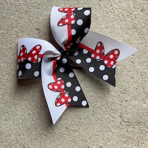 May include: A large hair bow featuring a black and white polka dot pattern with red accents. The bow has a red and white ribbon with a cartoon bow graphic. The bow is likely for a child.