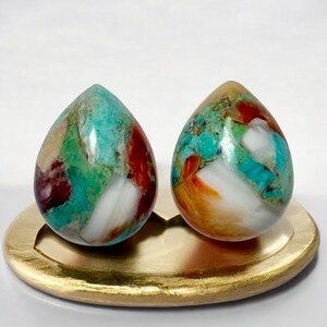 May include: Two teardrop-shaped, multi-colored gemstone earrings. The earrings are a mix of turquoise, white, orange, and red.