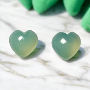 May include: Two heart-shaped green jade stones. The stones are smooth and polished, with a light green color.