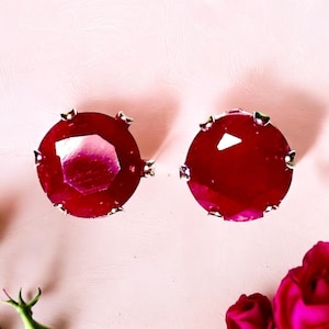 May include: A pair of ruby red earrings with a silver setting. The earrings are round and have a faceted design.