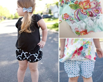 May include: Two girls wearing different styles of shorts. One girl is wearing black and white checked shorts with a black shirt. The other girl is wearing blue and white patterned shorts with a floral top.