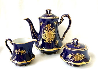 May include: A cobalt blue porcelain tea set with gold floral accents. The set includes a teapot, creamer, and sugar bowl.
