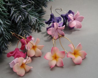 May include: Two pairs of hoop earrings featuring floral charms. One pair has purple and light pink flowers, while the other pair features vibrant pink and gradient pink-to-yellow plumeria-style blossoms attached to thin gold-toned metal hoops.